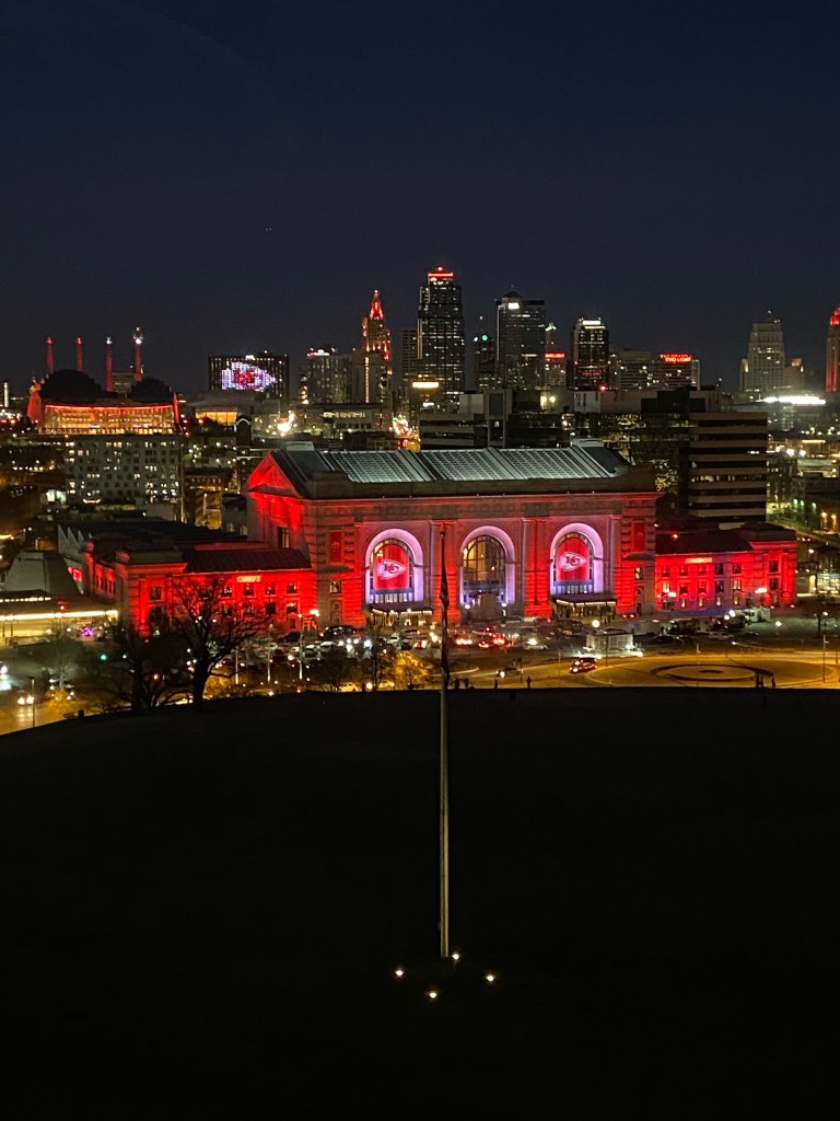 Photo of Union Station and downtown Kansas City at night as seen from the Liberty Memorial. Union Station is lit up in red, white and gold on this occasion, the team colours of the Kansas City Chiefs, the local football team and Superbowl winners